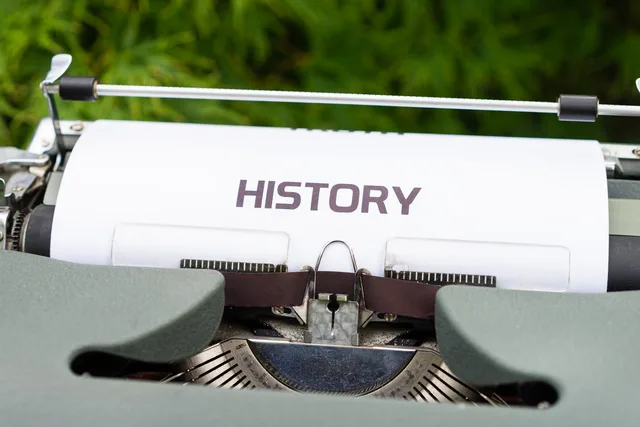 Close-up of a vintage typewriter with a paper labeled 'History' in an outdoor setting. Checking version history before choosing a document platform