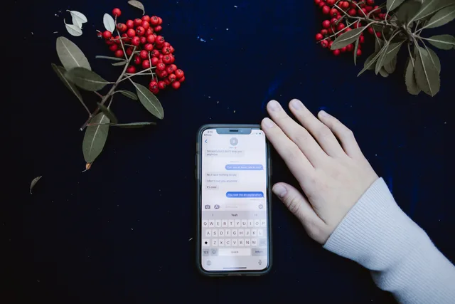 A hand beside a smartphone showing a text message conversation, surrounded by red berries. Comparing threaded conversations across chat tools