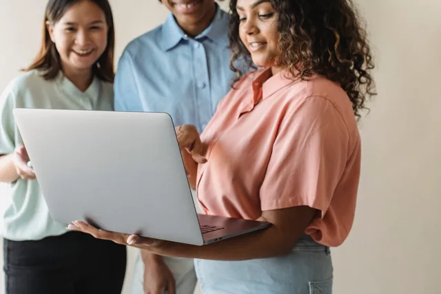 Three diverse women engaging in teamwork on a laptop indoors. Team knowledge and wiki software